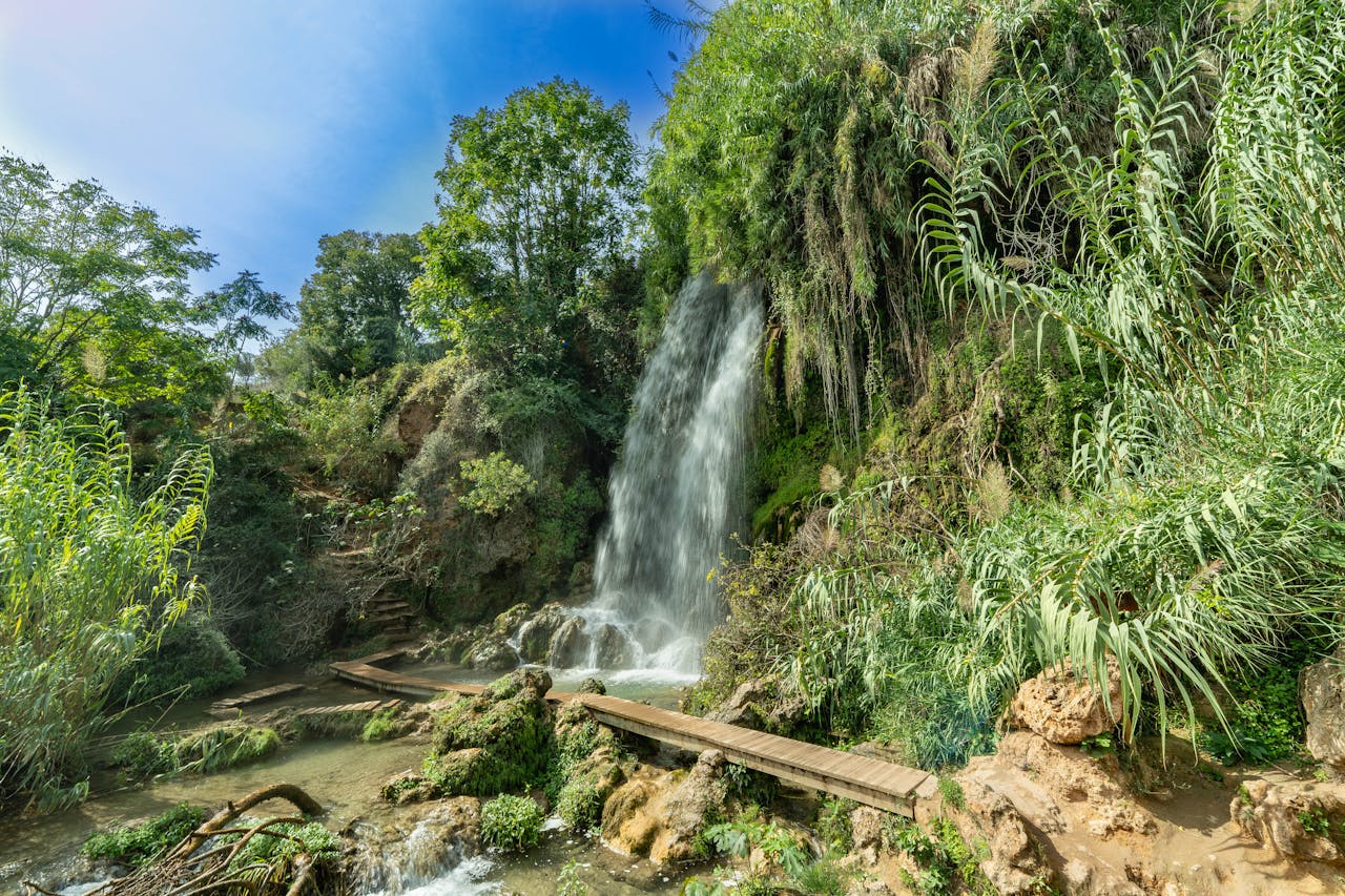 Beautiful waterfall surrounded by lush greenery in Anna, Spain, under a clear blue sky.